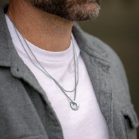Man wearing a silver necklace with a white shirt and gray jacket.