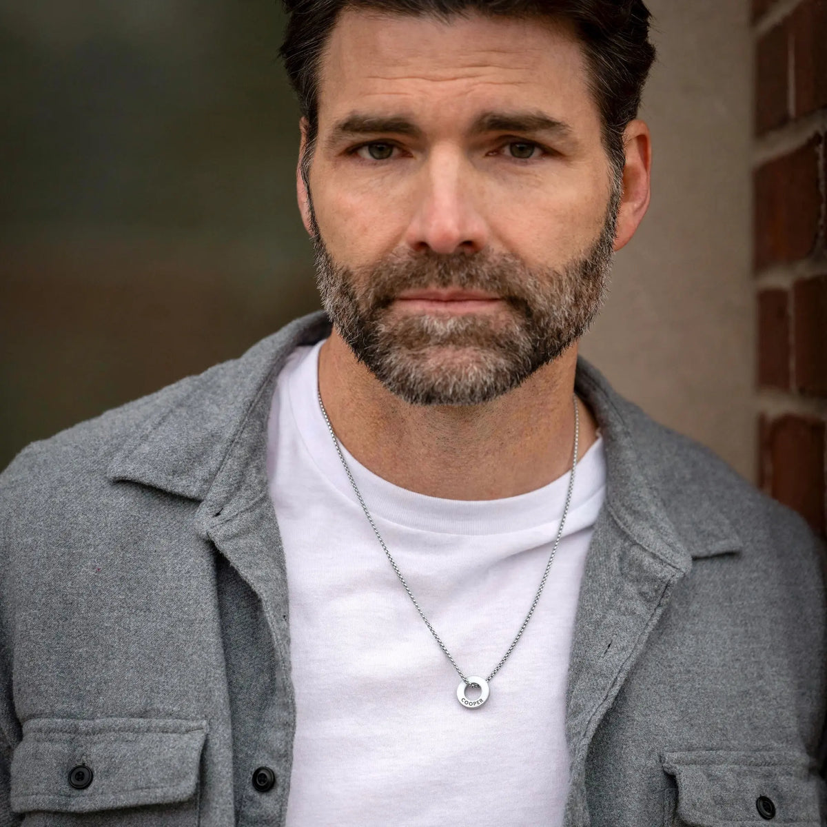 Man wearing a gray jacket over a white shirt with a brick wall background
