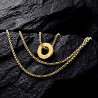 A gold chain necklace with a circular ring pendant engraved with the brand name 'CALVIN', displayed on a dark, textured rock surface.