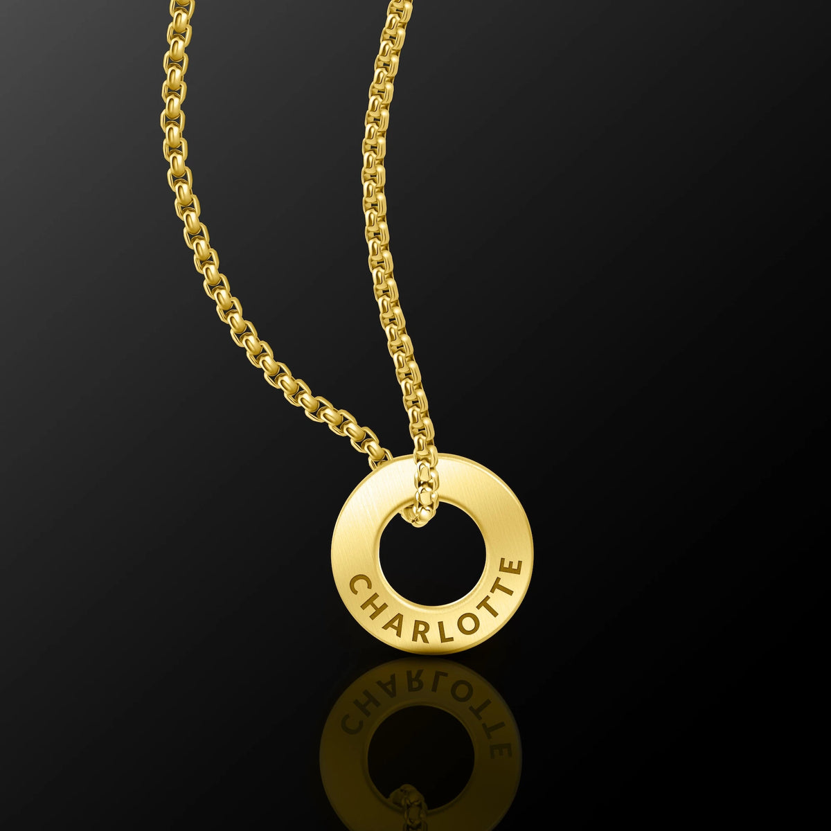 A gold-tone necklace featuring a circular ring pendant engraved with the name 'CHARLOTTE', suspended from a matching chain against a dark reflective background.