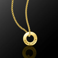A gold-tone necklace featuring a circular ring pendant engraved with the name 'CHARLOTTE', suspended from a matching chain against a dark reflective background.