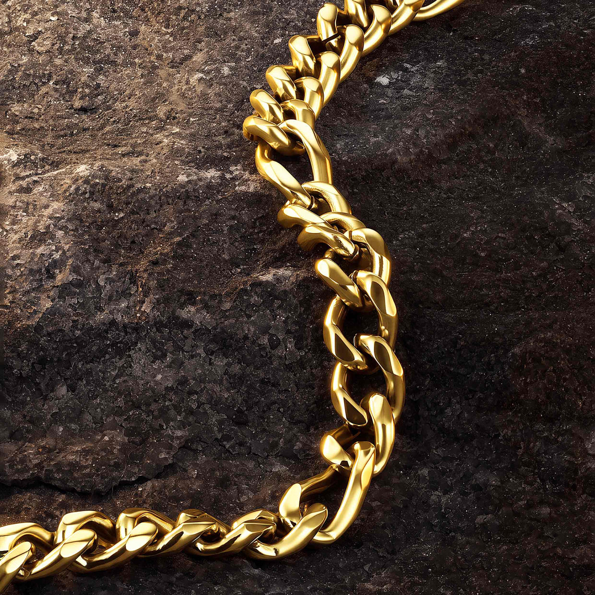 A close-up of a thick, polished gold figaro link chain draped over a dark, textured rock surface.