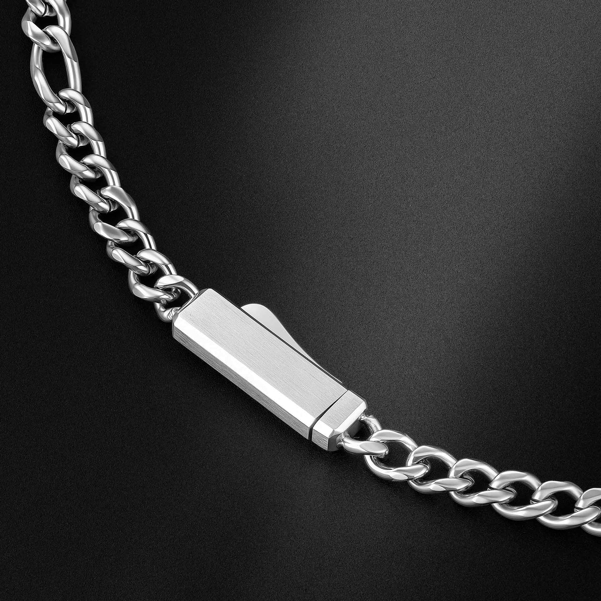 A close-up of a silver-toned metal chain necklace with a polished rectangular clasp, photographed on a dark black background.