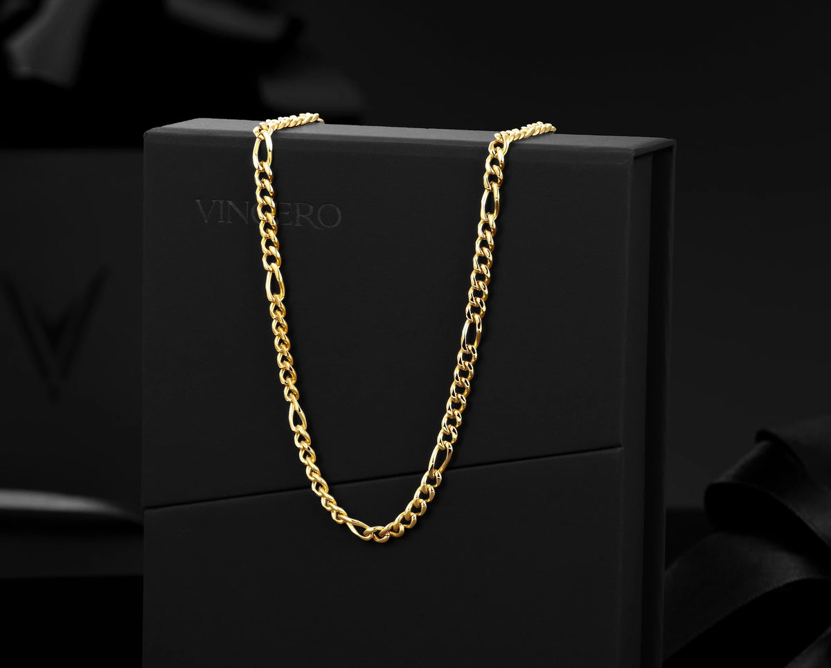 A gold-tone Figaro chain necklace draped over a black presentation box, with the brand name VINcero subtly printed on the box.