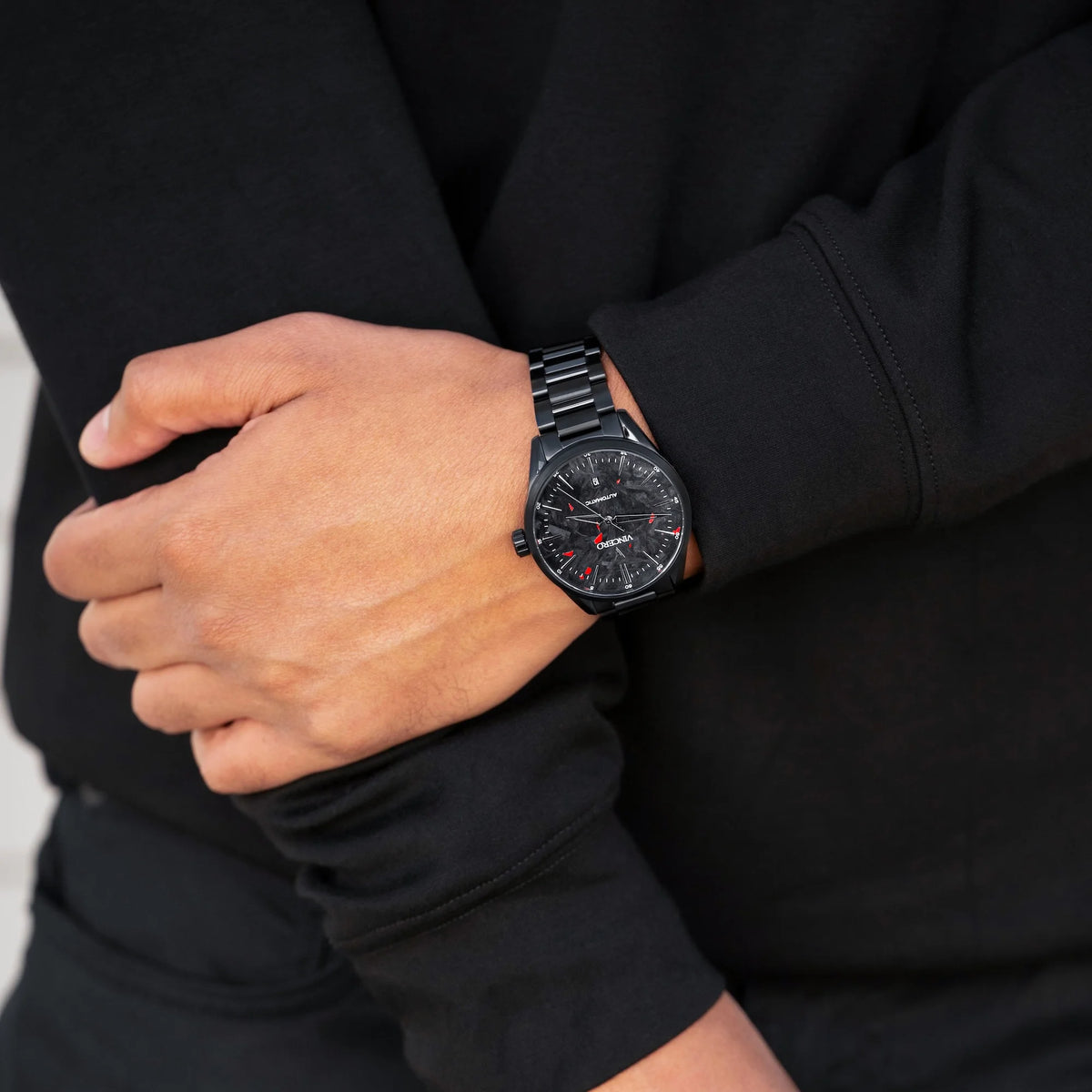 Person wearing a black watch with a detailed face on a plain background