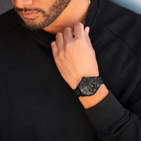 Man wearing a black watch with a detailed face, dressed in a black outfit.