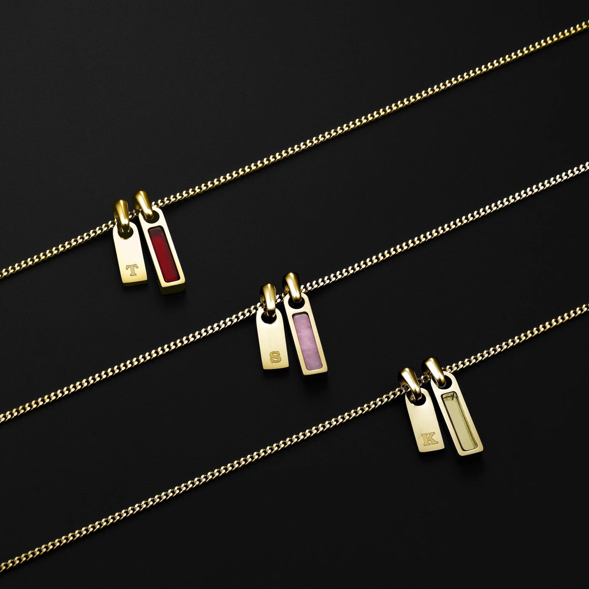 Three gold necklaces with small rectangular pendants on a black background