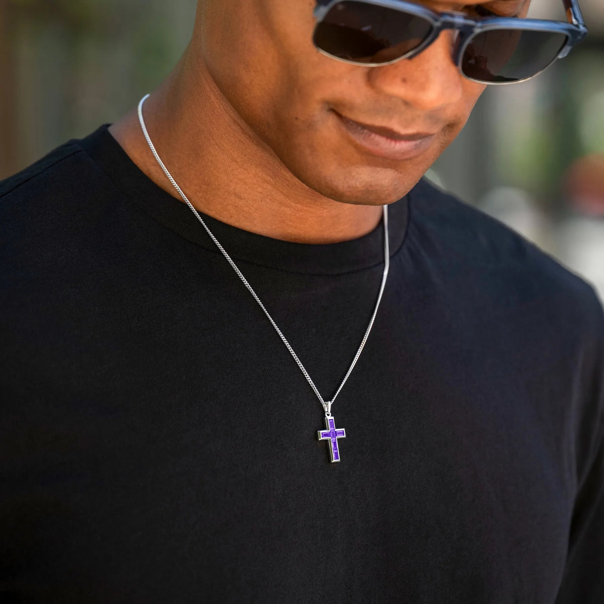 Man wearing a black shirt and sunglasses with a necklace featuring a cross pendant.