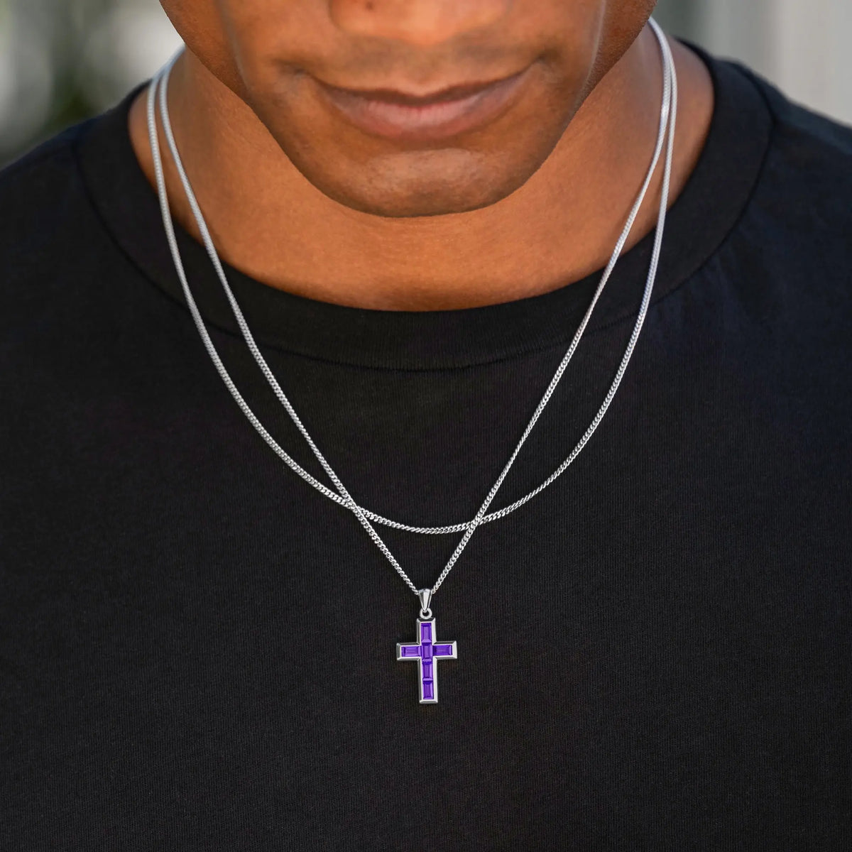 Man wearing a black shirt with a silver necklace featuring a purple cross pendant.