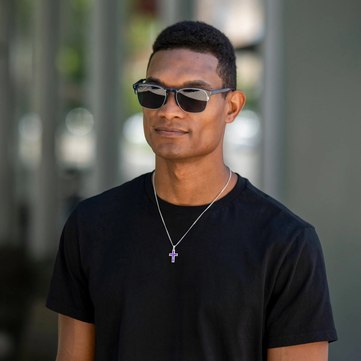 Man wearing sunglasses and a black t-shirt with a blurred background