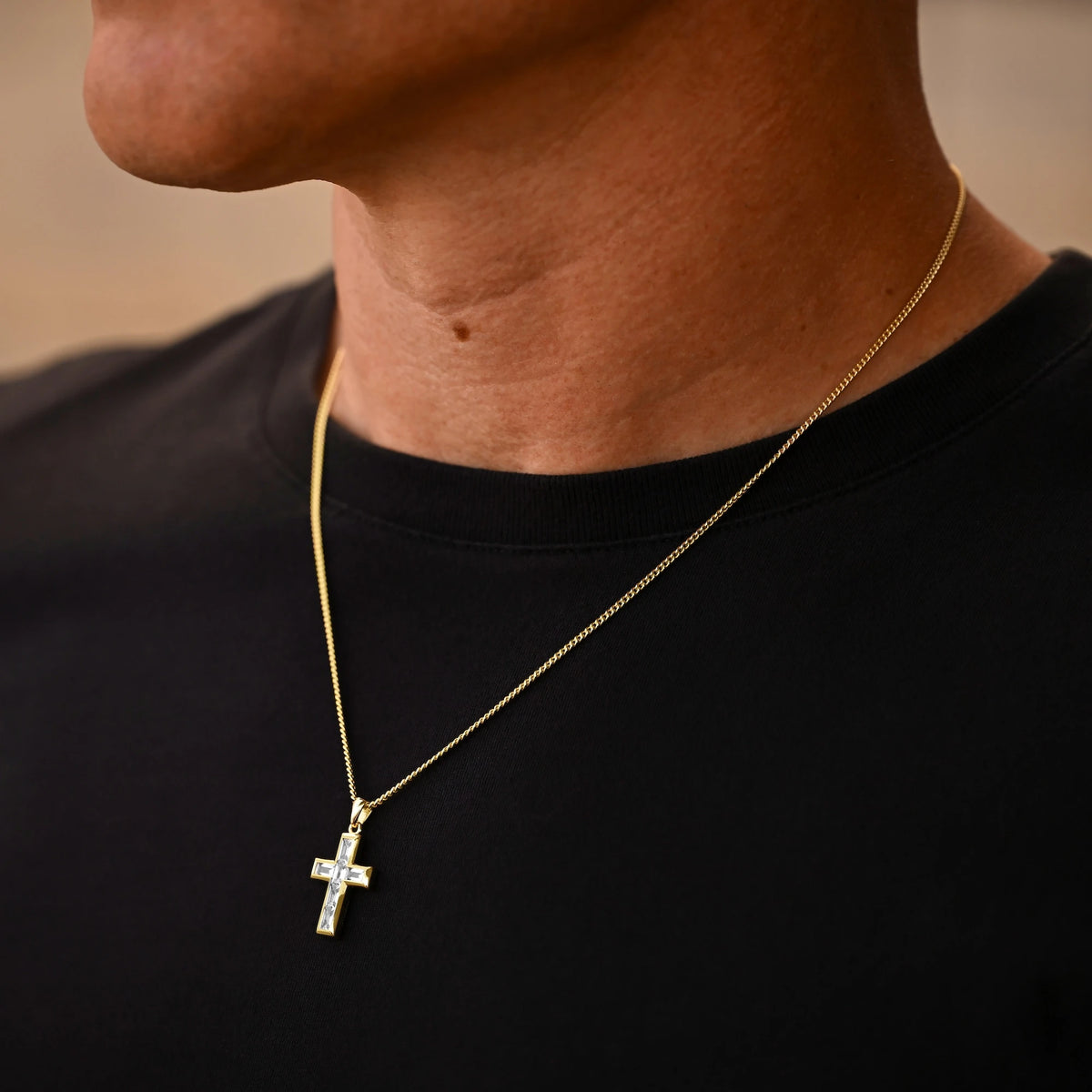 Gold necklace with a cross pendant on a person wearing a black shirt.