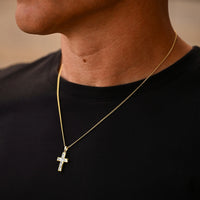 Gold necklace with a cross pendant on a person wearing a black shirt.
