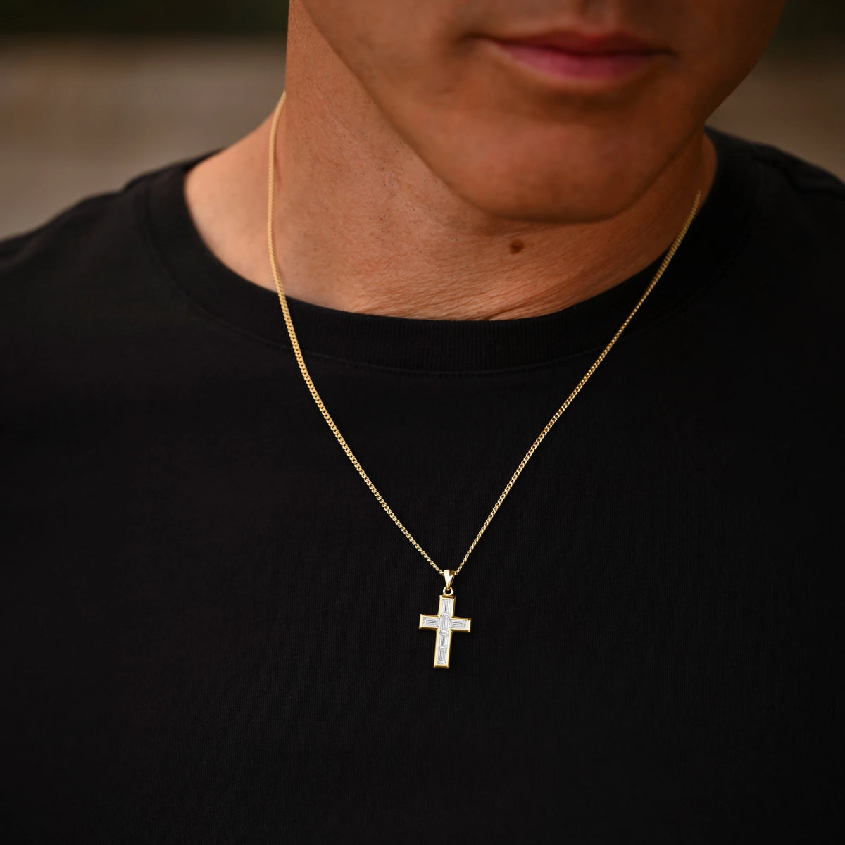 Person wearing a gold necklace with a cross pendant on a blurred background