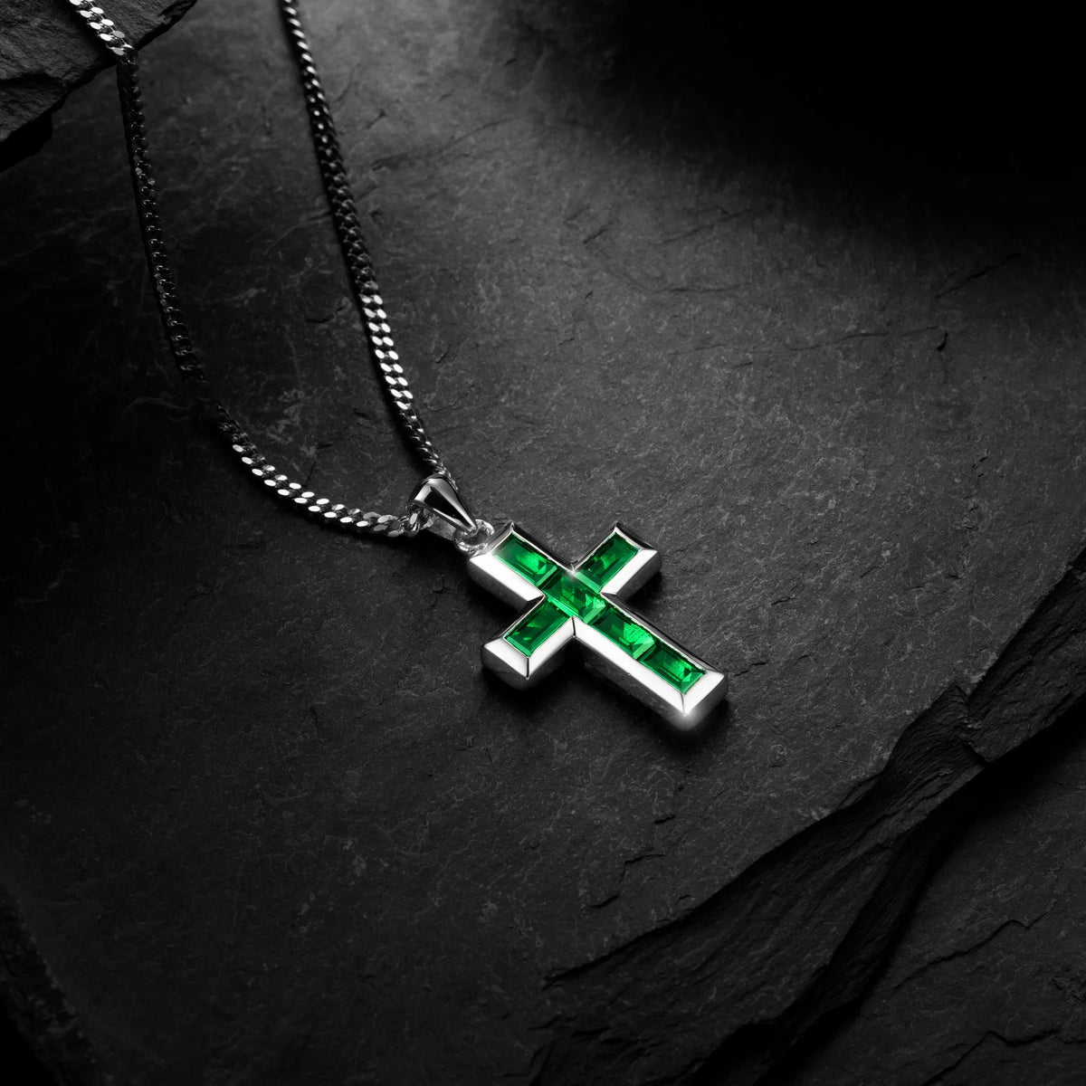 Silver cross pendant with red stones on a chain against a black background