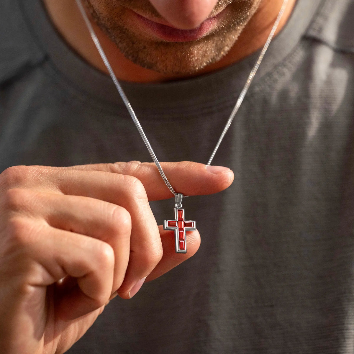 Person holding a silver cross pendant with red accents