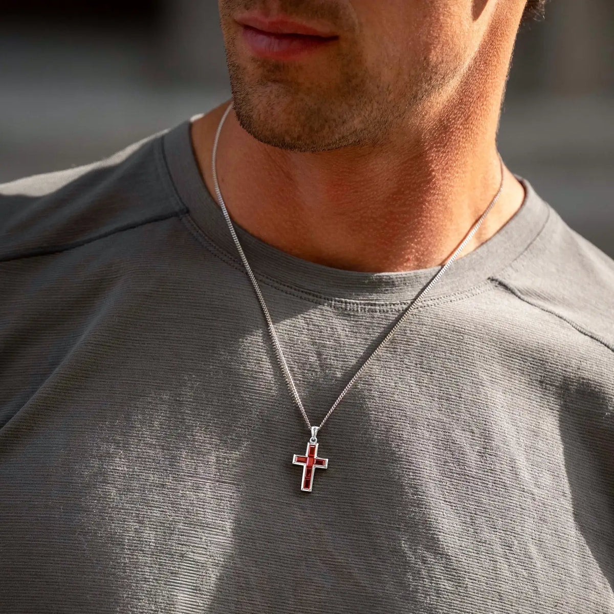 Man wearing a gray shirt with a necklace featuring a cross pendant.