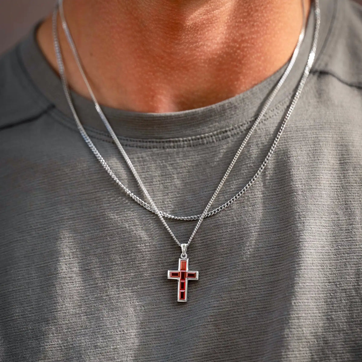 Person wearing a gray shirt with a silver necklace featuring a cross pendant.