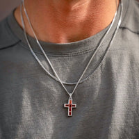 Person wearing a gray shirt with a silver necklace featuring a cross pendant.