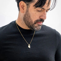 Man wearing a gold necklace with a small pendant on a plain background