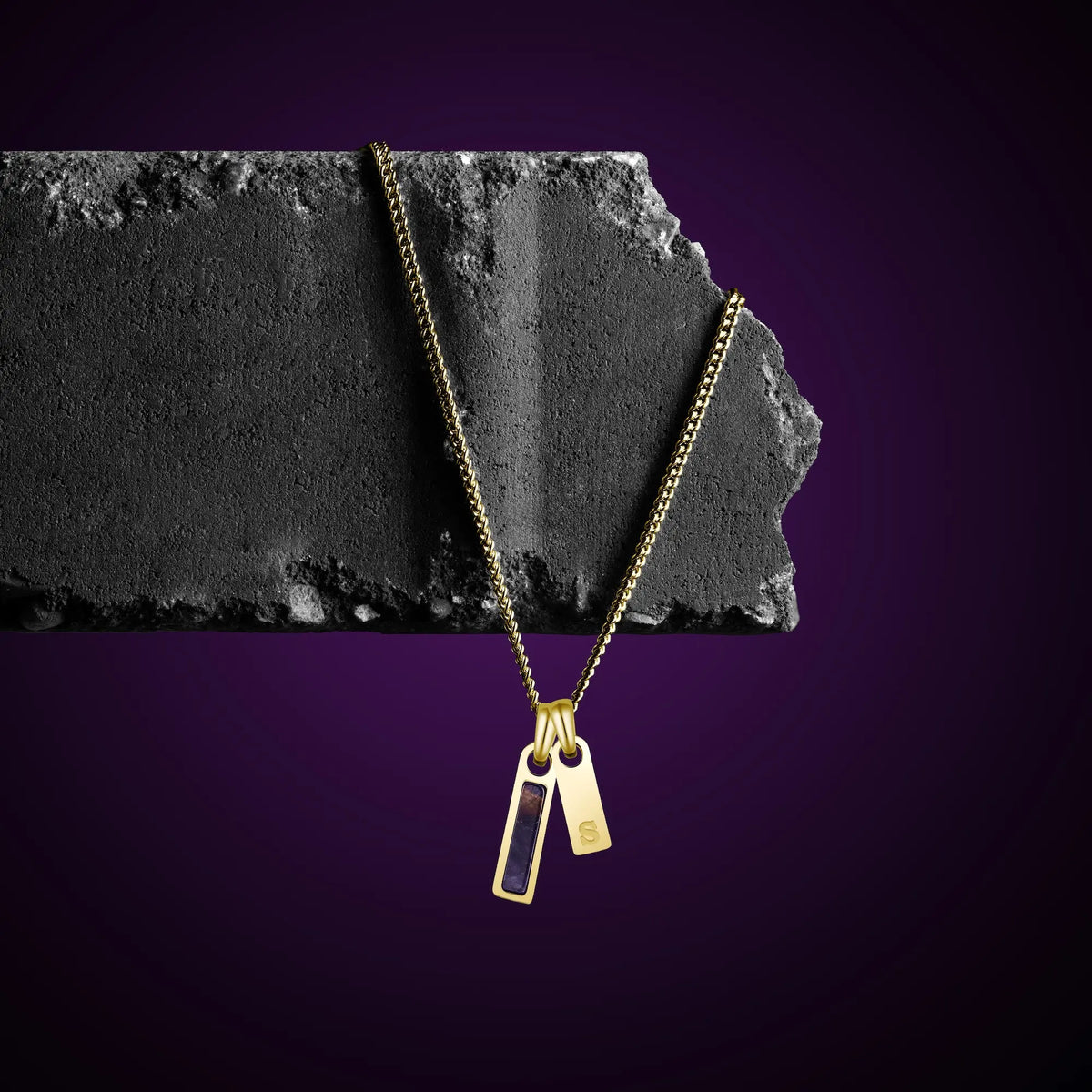 Gold necklace with two pendants on a dark stone surface against a purple background