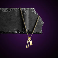 Gold necklace with two pendants on a dark stone surface against a purple background
