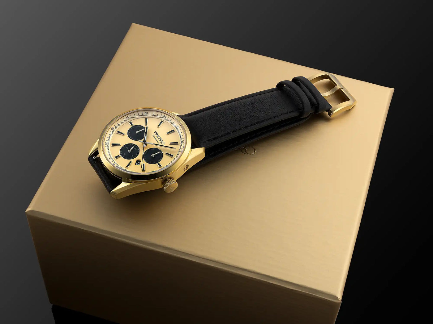 Gold wristwatch with black strap on a gold box against a dark background