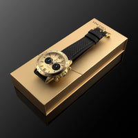 Gold watch with black strap on a gold box against a dark background