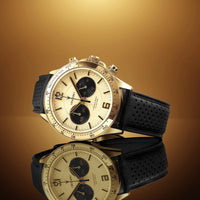 Luxury watch with black strap and gold case on a reflective surface with a warm brown background
