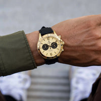 Gold watch with black strap on a wrist, blurred background