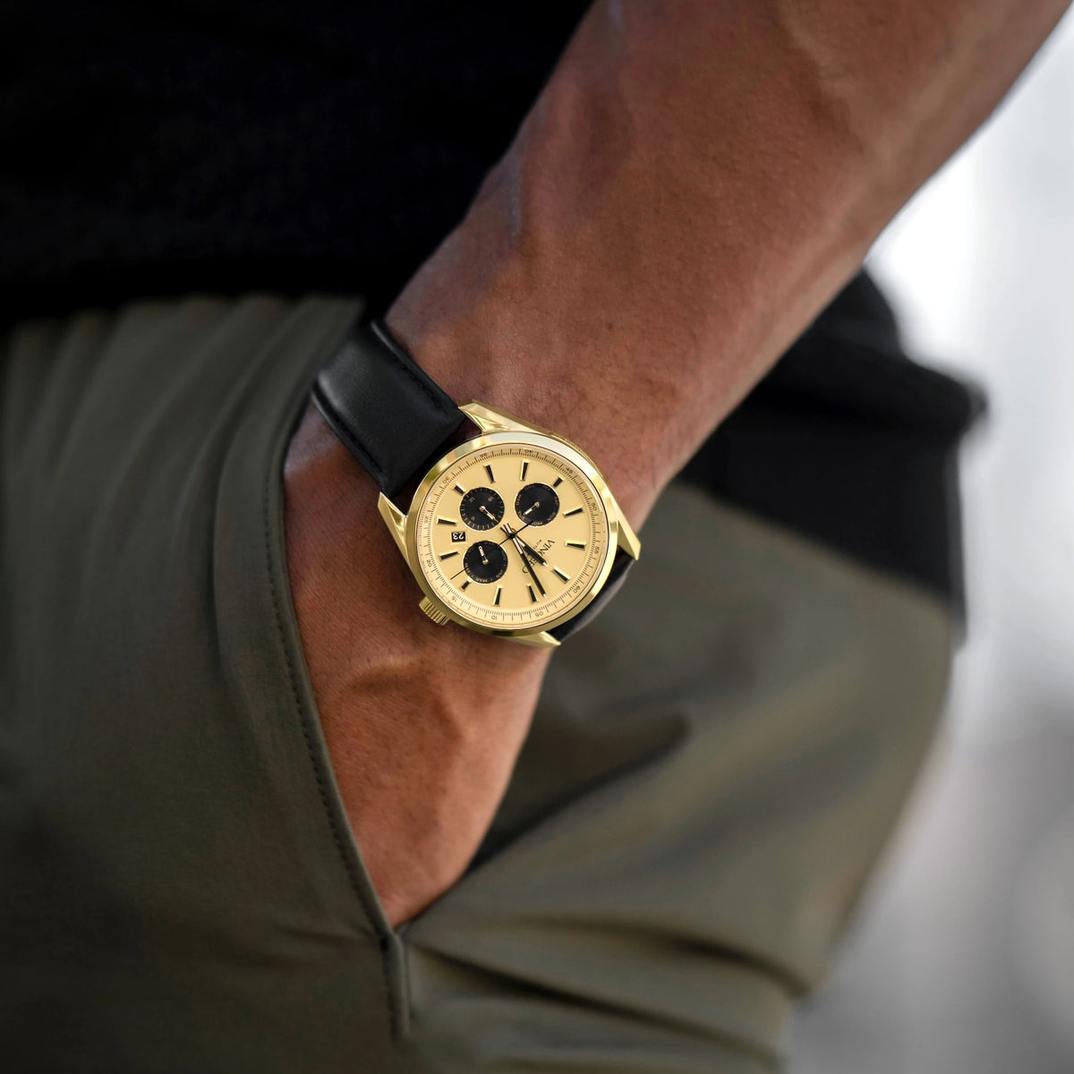 Gold watch with black strap on a wrist, blurred background
