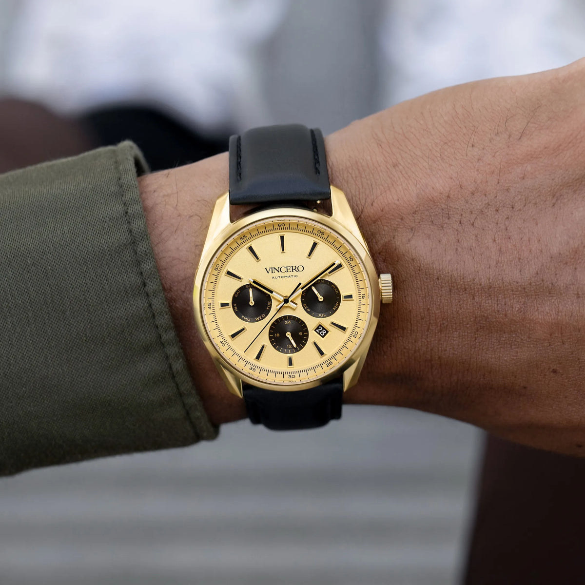 Gold wristwatch with black strap on a person's wrist, brand 'Vincero' visible.