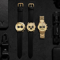 Three gold watches with black straps on a dark textured surface.