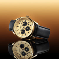 Gold wristwatch with black leather strap on a gradient brown background