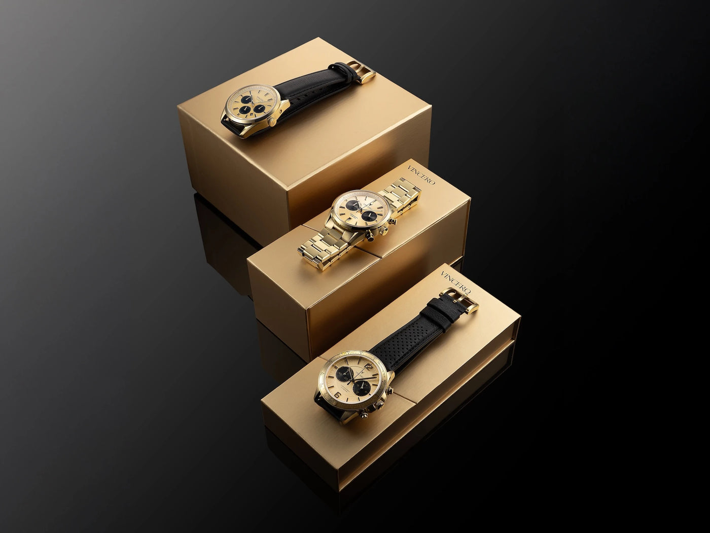 Three gold watches with black straps on cardboard boxes against a dark background