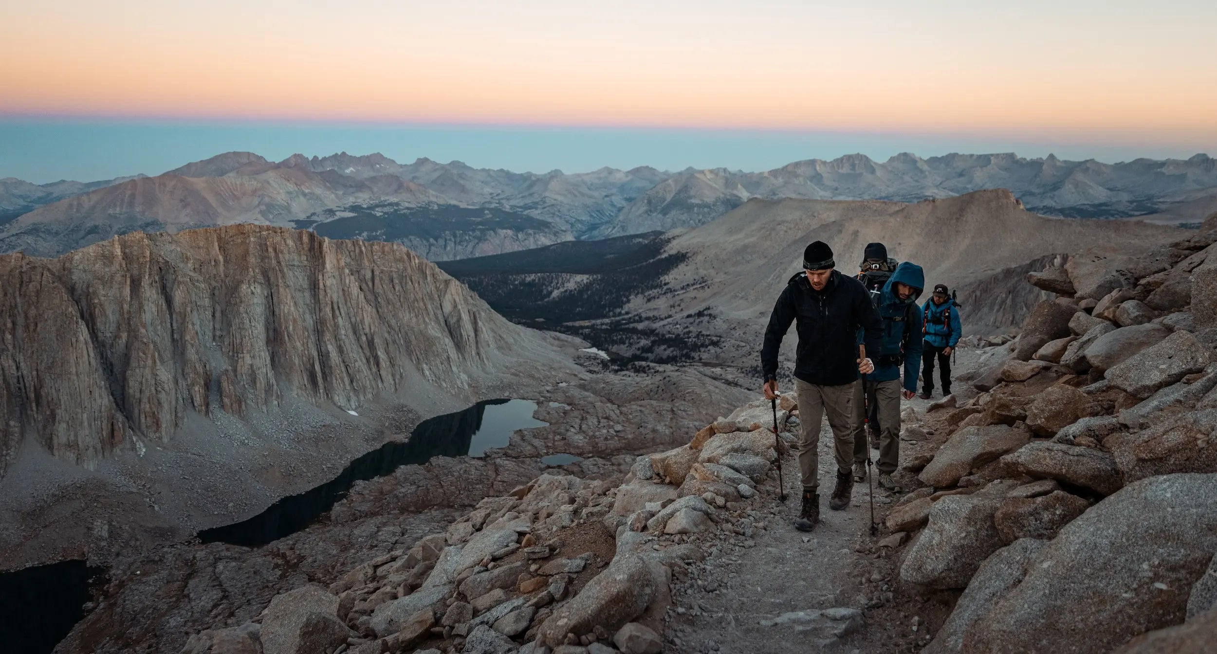Men hiking along a rocky ridge with a canyon in the background. 