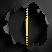 A gold ID chain bracelet with a polished rectangular plate in the center, shown hanging vertically against a dark background with a torn-paper effect revealing a black interior.