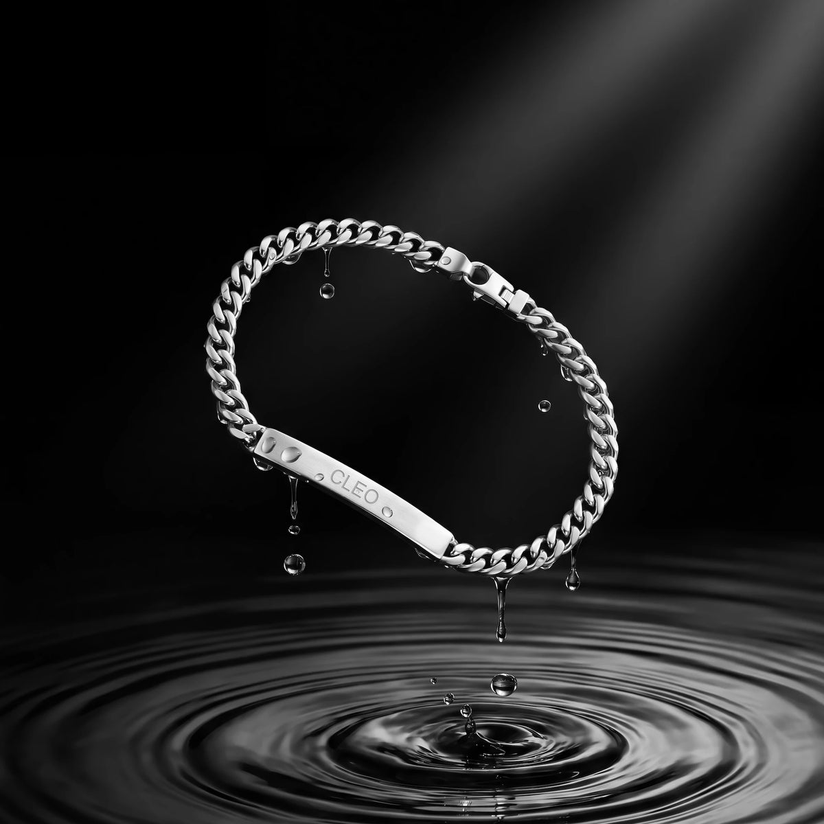A silver-toned stainless steel chain bracelet with a flat ID bar engraved with the brand name 'CLEON', suspended over a water ripple on a dark background.