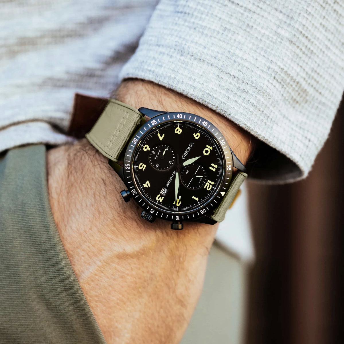 Close-up of a person wearing a watch with a beige strap on a neutral background