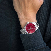 Wrist wearing a silver watch with a red face against a dark background