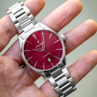 Silver watch with a red face held in a hand against a neutral background