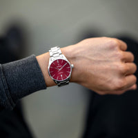 Person wearing a watch with a red face and silver strap on a blurred background