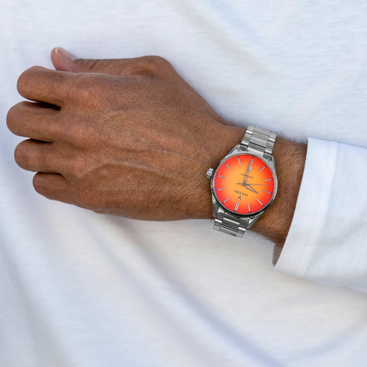 Man with white shirt wearing a Solar Flare Edition watch, featuring a orange face, stainless steel casing, and steel band.