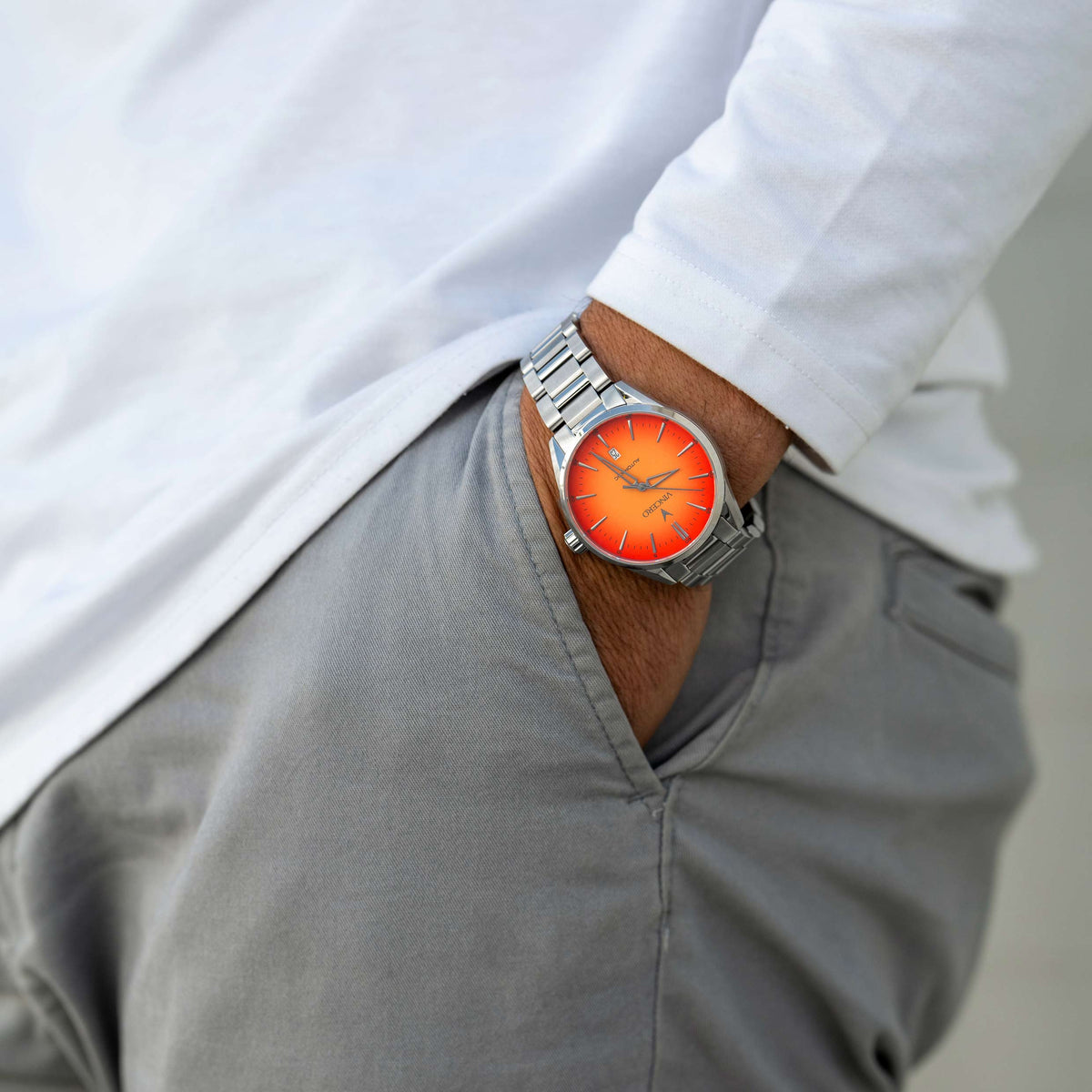 Man with hand in pocket wearing a Solar Flare Edition watch, featuring a orange face, stainless steel casing, and steel band.