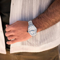 Person wearing a silver watch with a white shirt and brown pants
