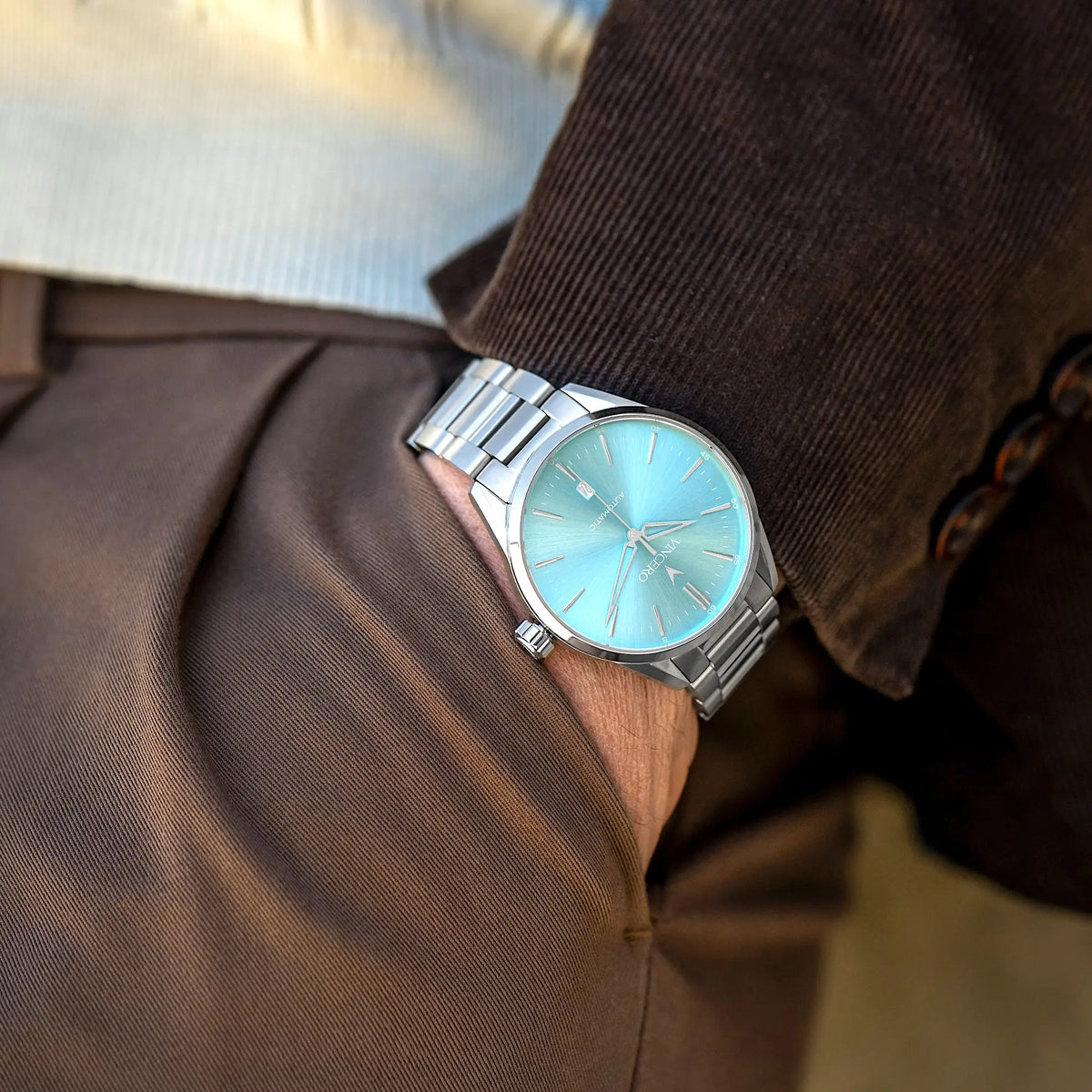 Silver watch with a light blue face on a person wearing a brown coat.