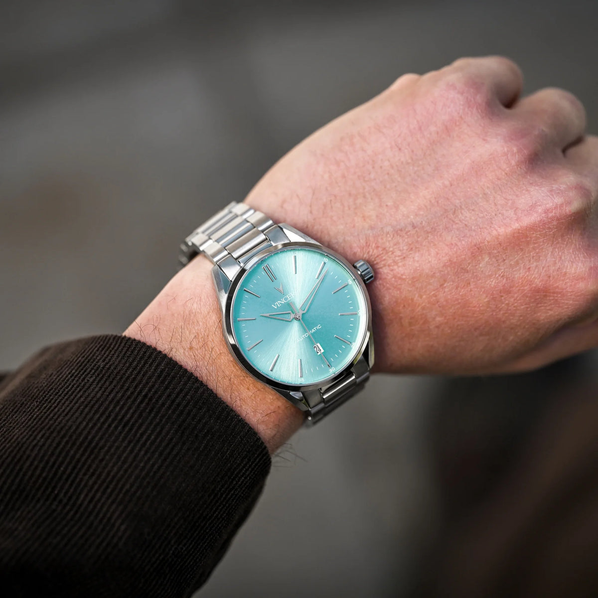Hand wearing a silver watch with a light blue face against a blurred background