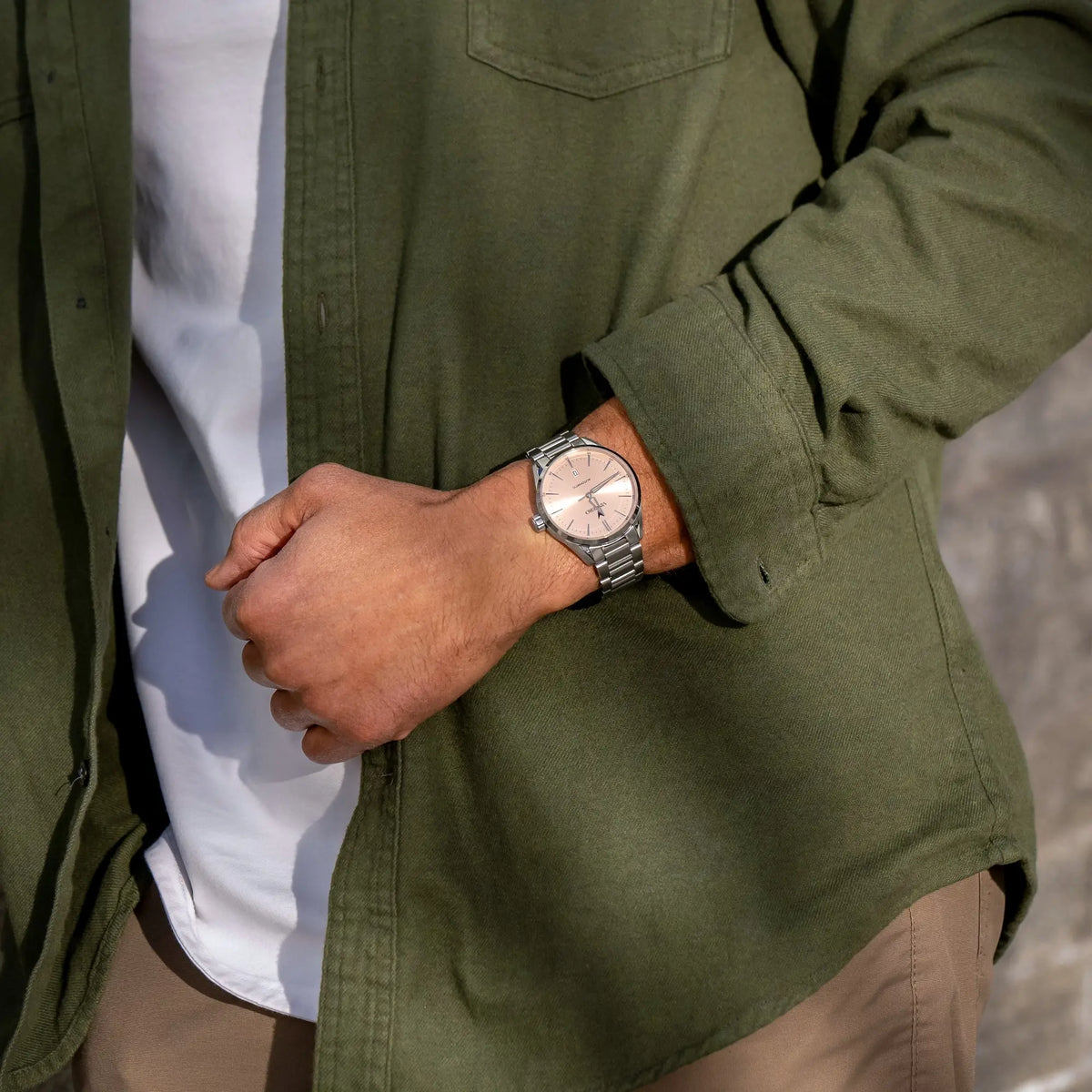 Person wearing a green jacket and white shirt with a watch on their wrist.
