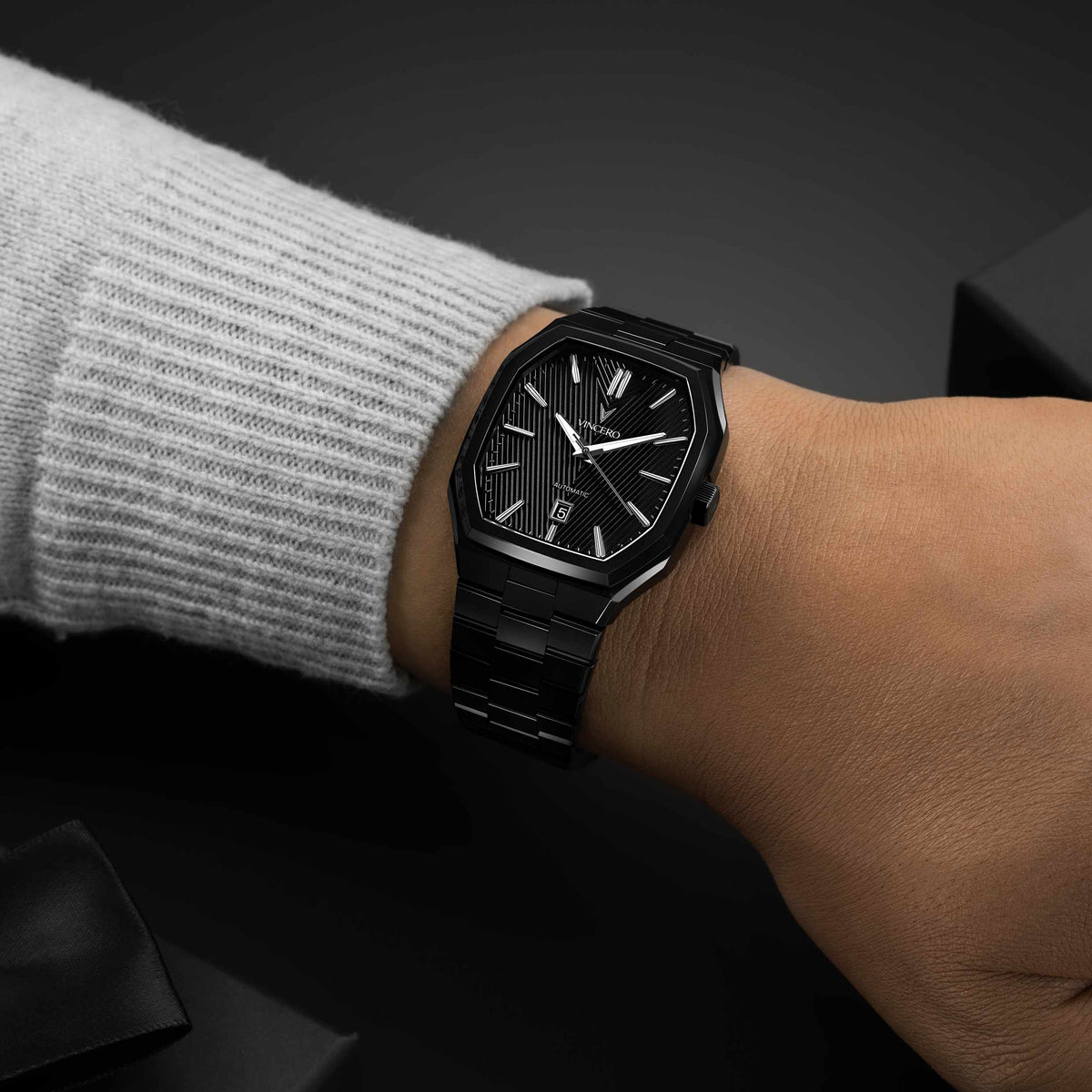 Black wristwatch on a person's wrist with a dark background