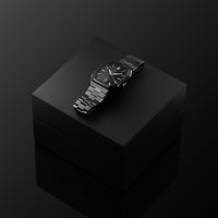 Black wristwatch on a reflective black surface with a dark background