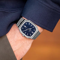 Person wearing a stylish watch with a blue face and silver case on a blurred background